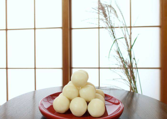 Tsukimi dango on a red serving plate, sitting on a wooden table with a shoji door and susuka grass in the background.